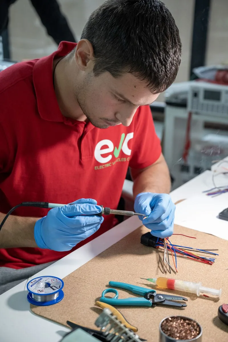 Technician soldering a wiring harness connector at the bench.